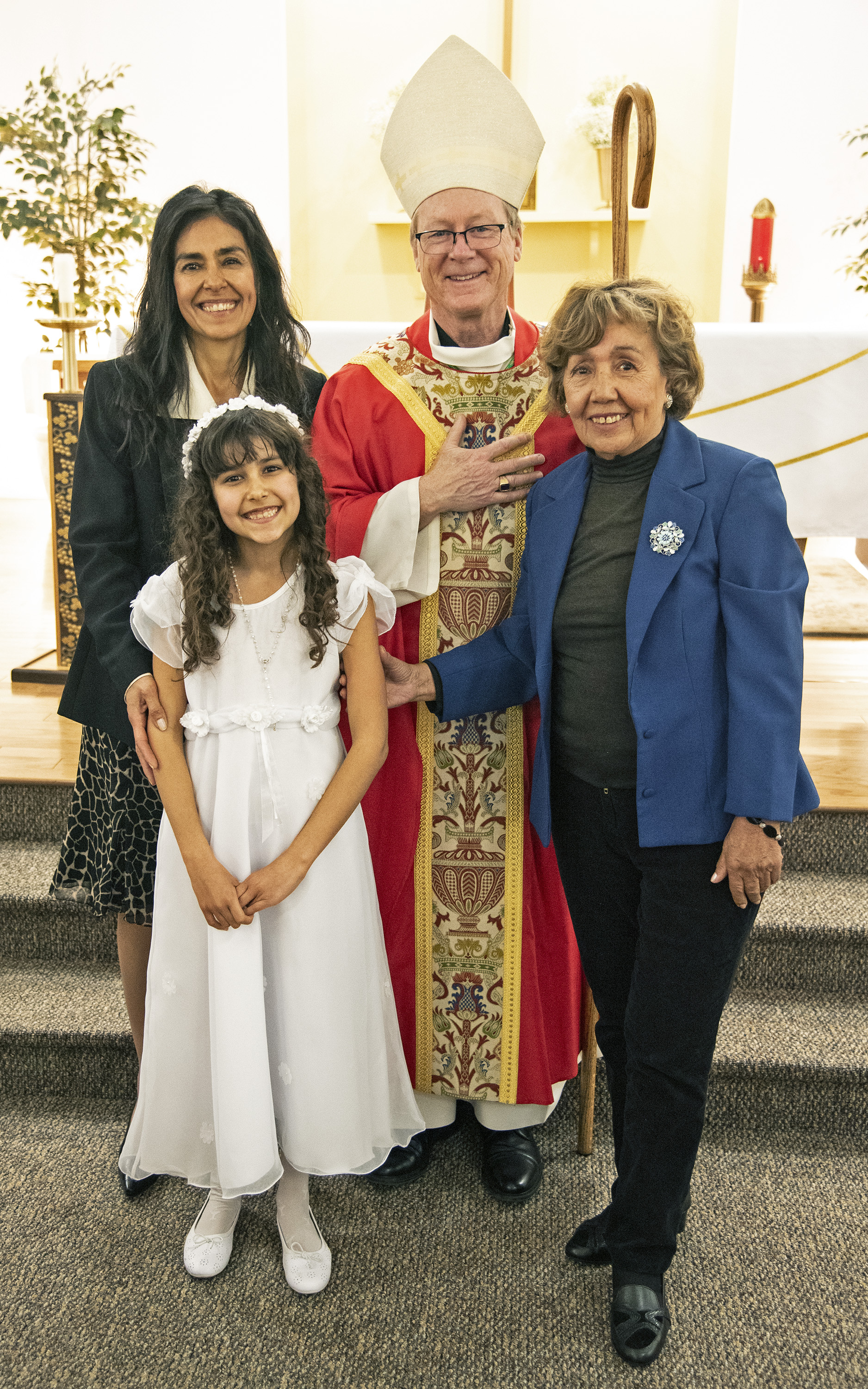 girl pictured with her mother, grandmother and a bishop after completing her first Communion