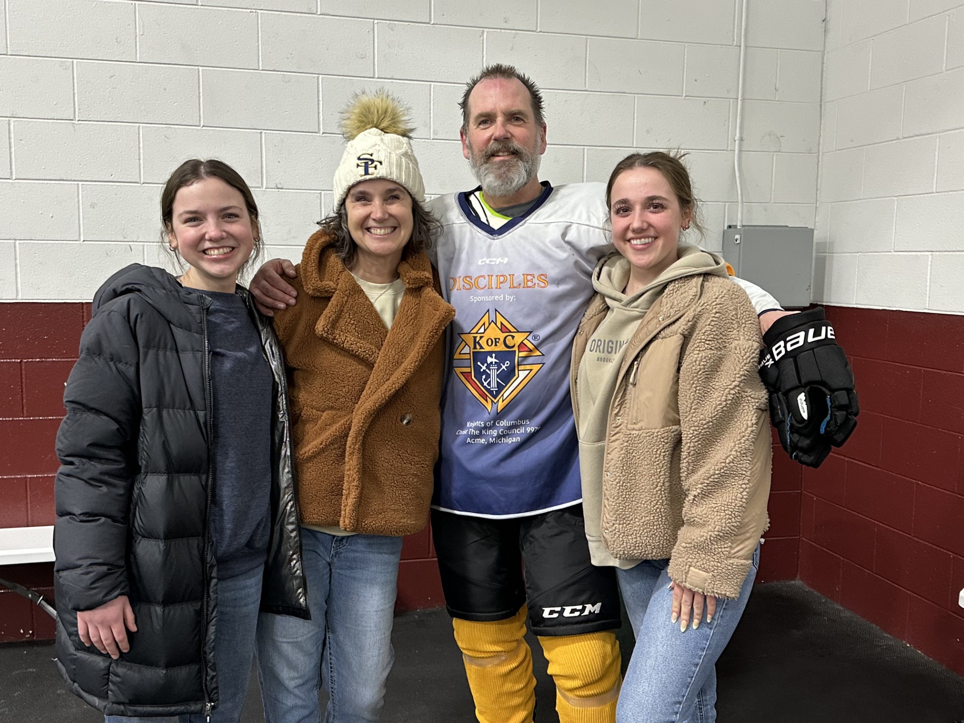 Mom, 2 daughters stand with their father after his hockey game. 