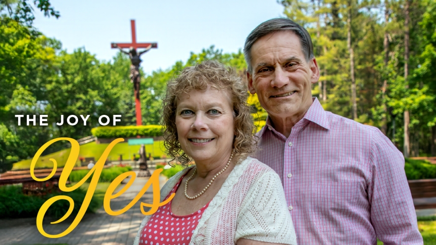 couple standing in front of cross with words The Joy of Yes
