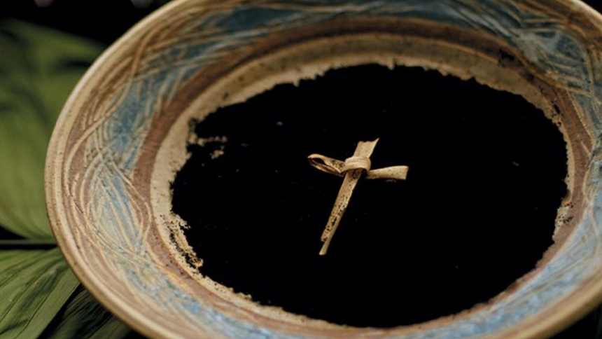 bowl of dirt with cross made out of a palm frond