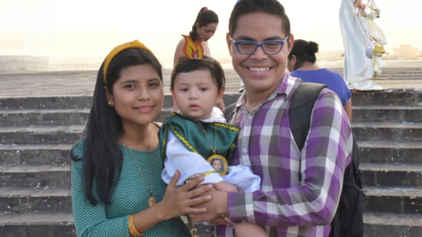 victoria, her son, and husband in front of concrete stairs with a religious statue